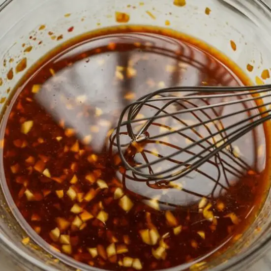Bowl of sweet and sour sauce freshly mixed on a white counter with ingredients around

