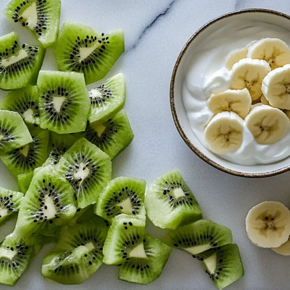 Chopped kiwi and banana next to yogurt on white counter