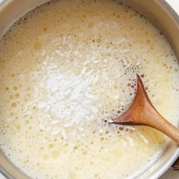 Coconut milk and sugar being mixed with bloomed gelatin for pudding.