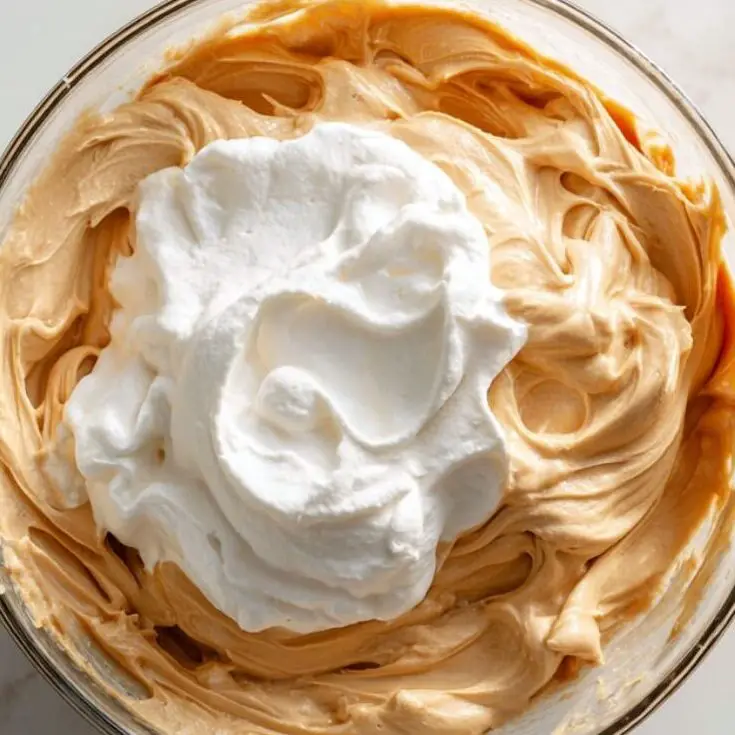 Folding whipped cream into peanut butter filling in a glass bowl