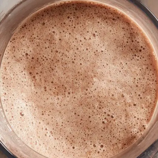 Blender jug open with spoon for checking smoothie consistency.