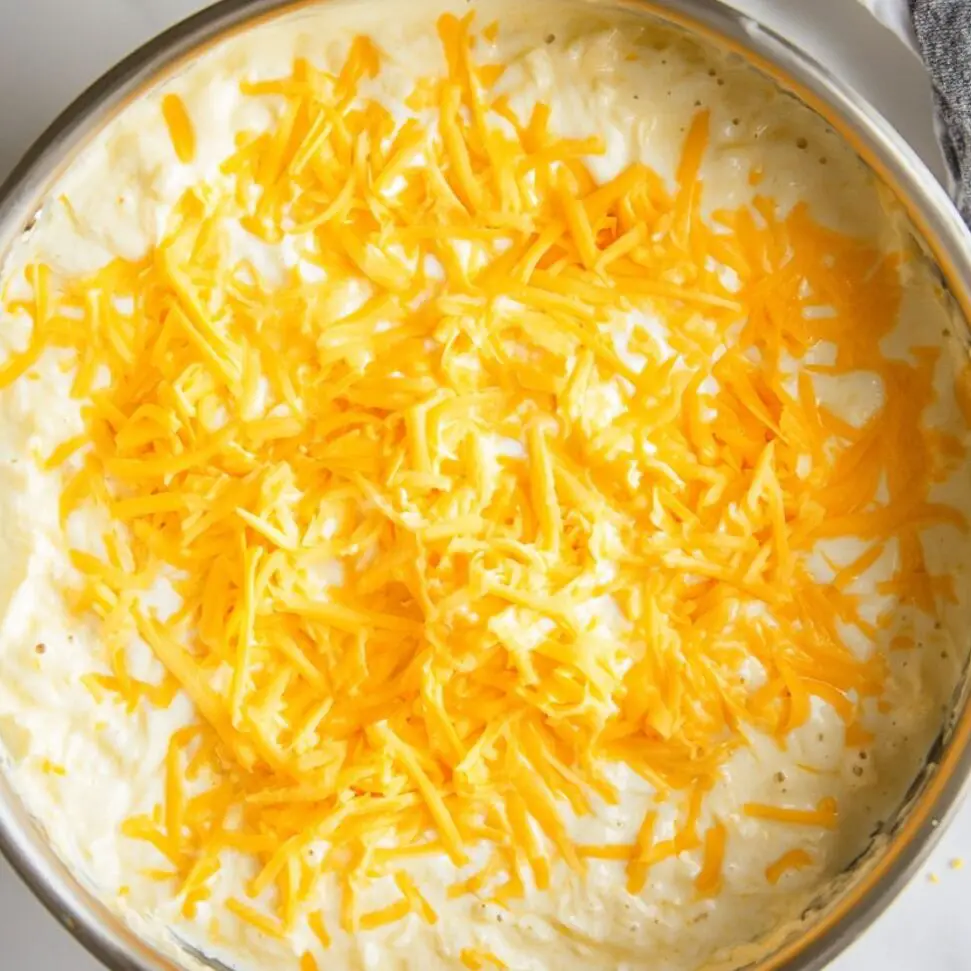 Shredded cheese melting into creamy sauce in a pot