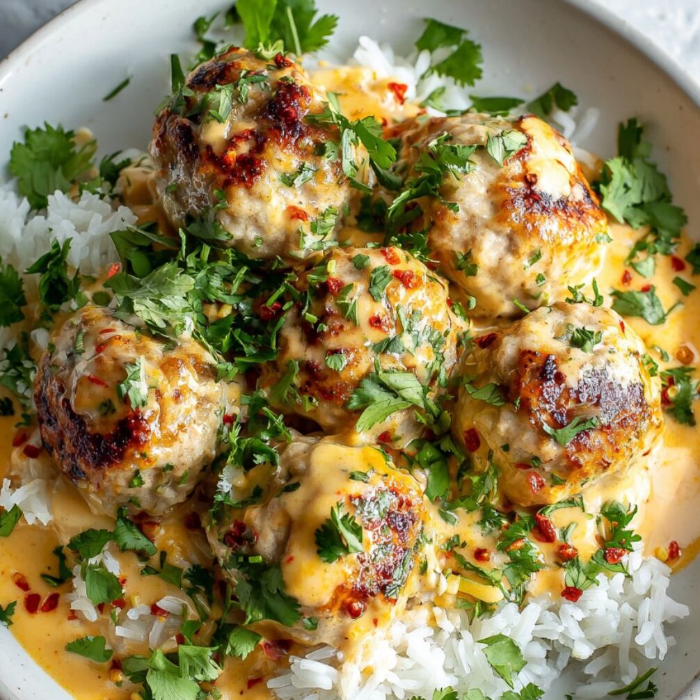 Bowl of creamy Thai coconut sauce next to plated meatballs on rice