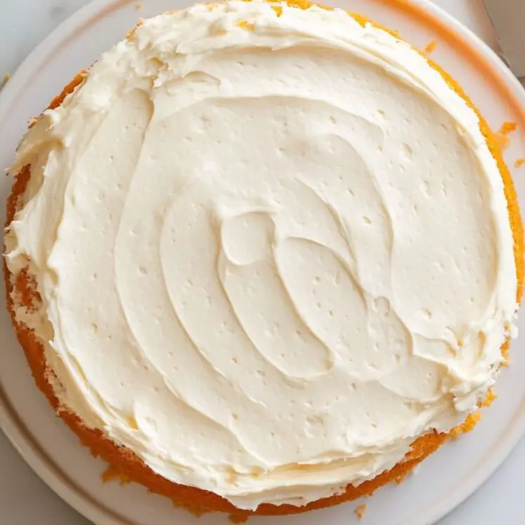 Frosting being spread between orange cake layers on a cake stand