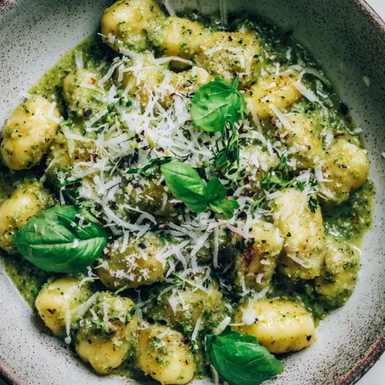 Finished pesto gnocchi in pan topped with Parmesan and spinach