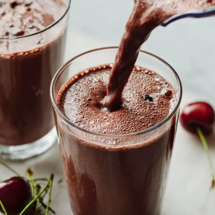 Pouring smoothie into glasses on marble counter.