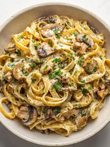 Creamy mushroom Alfredo pasta recipe served in a white bowl on a kitchen counter