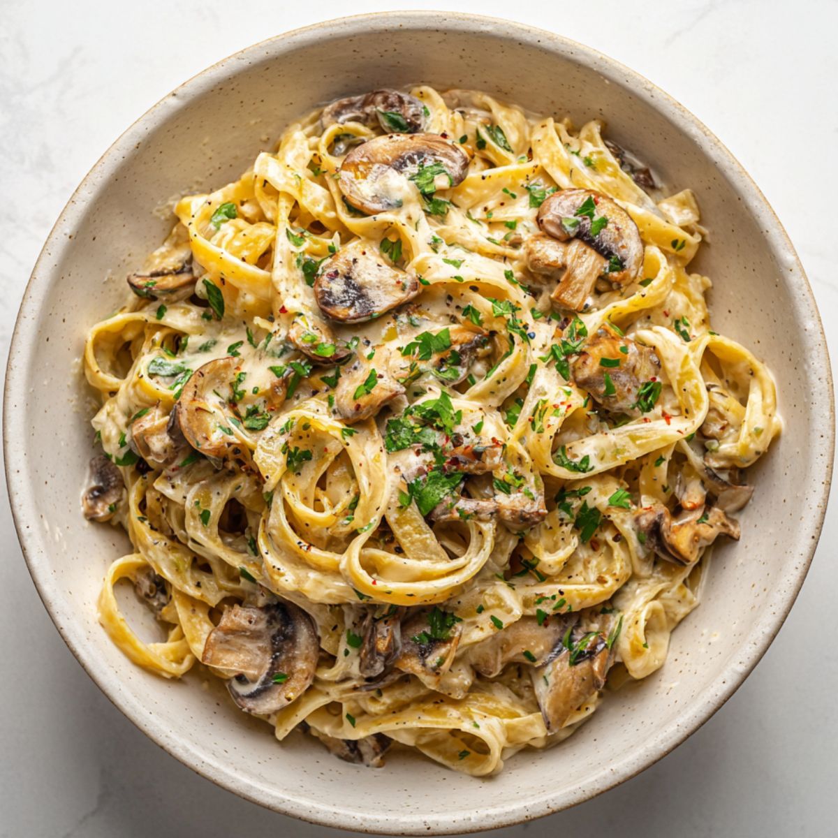 Creamy mushroom Alfredo pasta recipe served in a white bowl on a kitchen counter