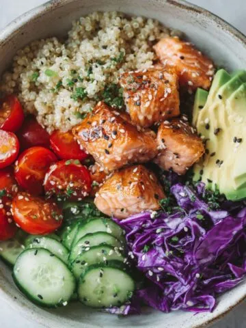 Salmon quinoa bowl recipe with fresh vegetables and avocado on a white counter
