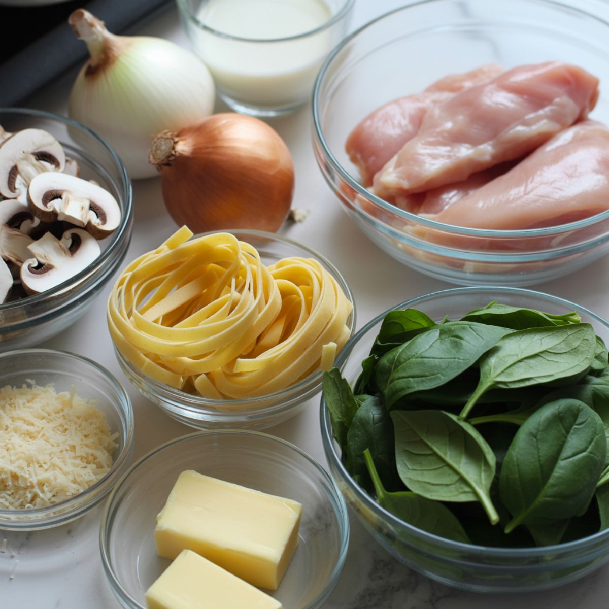 Overhead shot of ingredients for chicken tagliatelle including chicken, pasta, garlic, cream, parmesan, and herbs