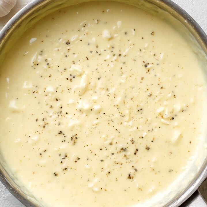 Alfredo sauce cooking in a saucepan with garlic and butter.