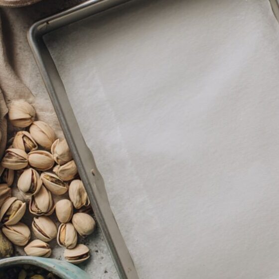 Kitchen setup with lined baking pan and chopped pistachios on a white counter, ready to bake