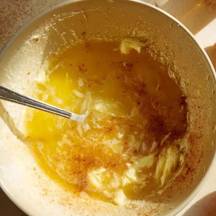 Mixing bowl with melted butter and brown sugar on a kitchen counter with egg shells and vanilla bottle