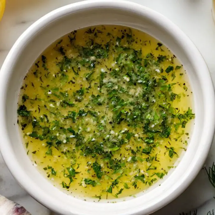 Lemon herb dressing in a small bowl with fresh herbs around it

