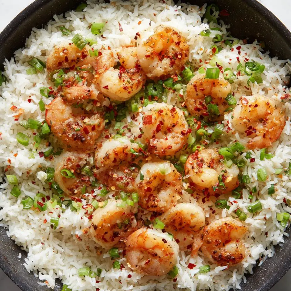 Close-up of shrimp and garnishes being mixed into rice in a skillet.