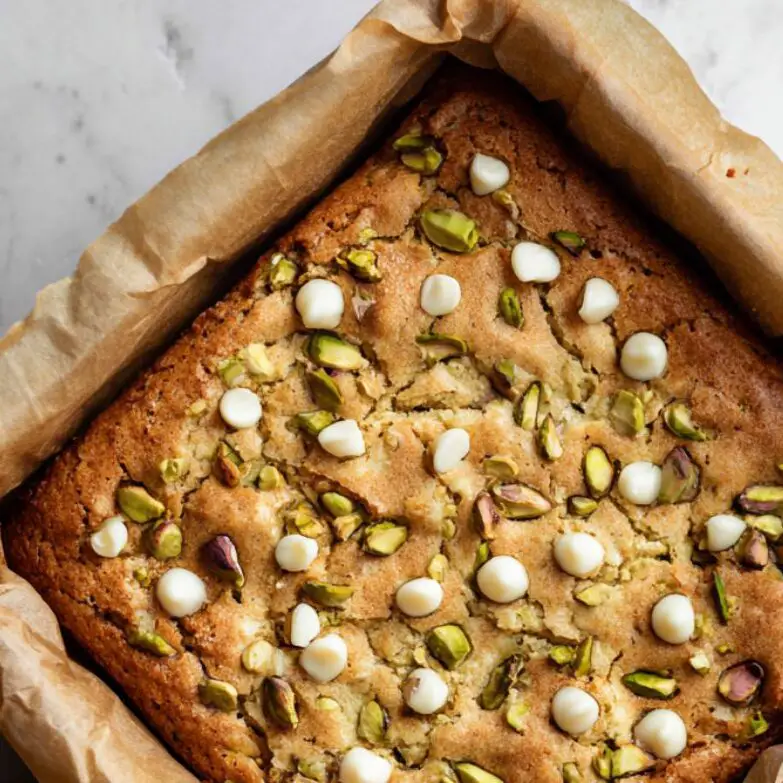 Freshly baked pistachio blondies in a pan lined with parchment, golden and slightly rustic
