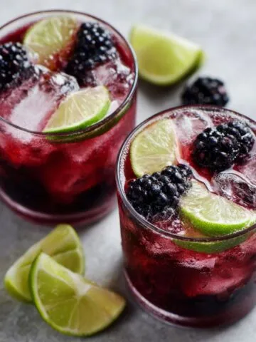 Glasses of blackberry limeade recipe on a white kitchen counter with lime slices and blackberries