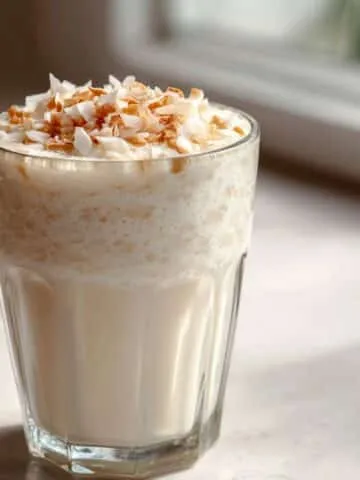 Coconut cream smoothie recipe in a glass with coconut flakes, on a white kitchen counter