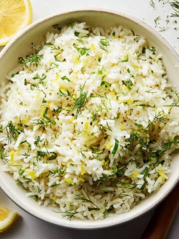 Fluffy lemon dill rice recipe in a bowl with lemon wedges on a white kitchen counter.