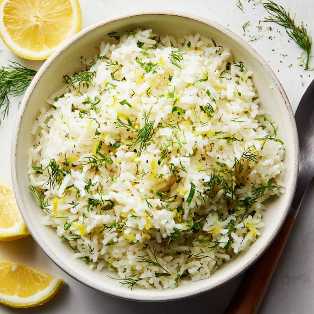 Fluffy lemon dill rice recipe in a bowl with lemon wedges on a white kitchen counter.
