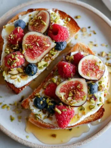 Ricotta and honey toast recipe on a plate topped with berries and nuts