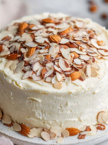 Homemade almond cream cake recipe with vanilla frosting and sliced almonds on top.