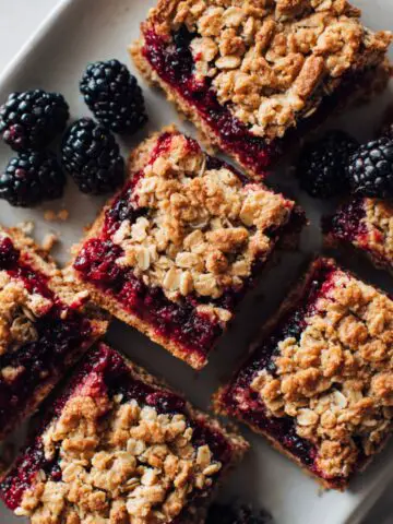 Freshly baked homemade blackberry oatmeal bars recipe on parchment with crumbly oat topping and juicy blackberry filling.