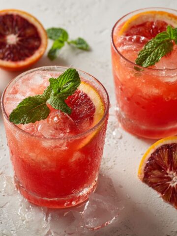 Glass of freshly squeezed blood orange juice recipe with mint on a white kitchen counter.