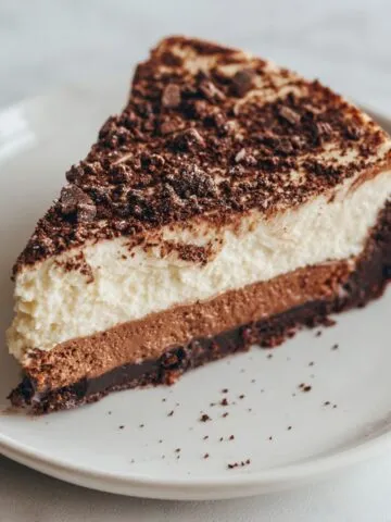 A slice of brownie bottom cheesecake recipe on a white plate, showing creamy top and fudgy base.