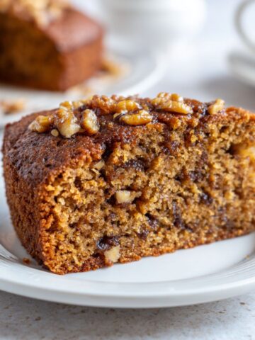 A close-up overhead shot of a homemade date and walnut cake recipe slice on a white plate, showing moist texture and rustic appeal.