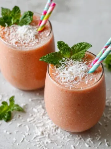 Freshly made pink guava smoothie recipe with mint and coconut on a white counter