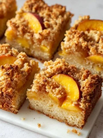 Overhead view of peach crumb cake recipe with golden topping and sliced peaches on a white counter.