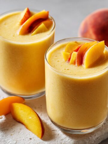 Overhead shot of a peach mango smoothie recipe in a glass with peach and mango slices on a white kitchen counter