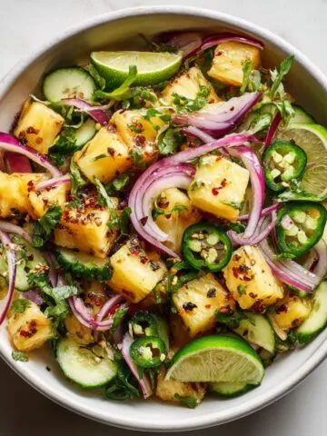 Top-down view of a pineapple cucumber salad recipe in a white bowl with tropical garnish on a white kitchen counter