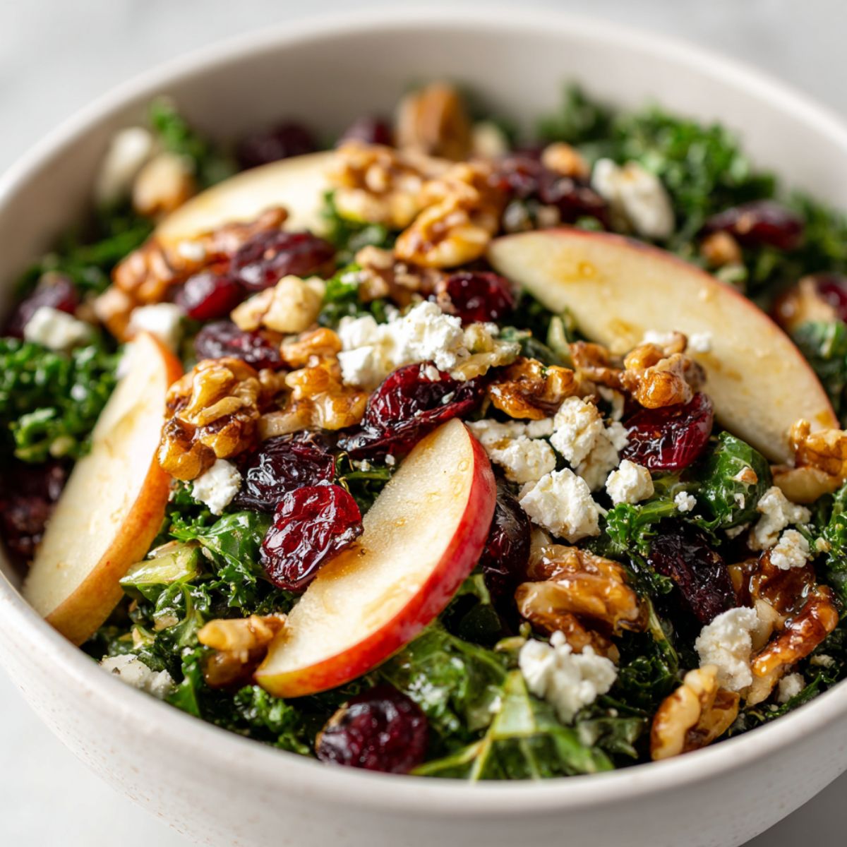 Overhead shot of Apple Walnut Kale Salad Recipe in a white bowl with apples, walnuts, cranberries, and goat cheese.

