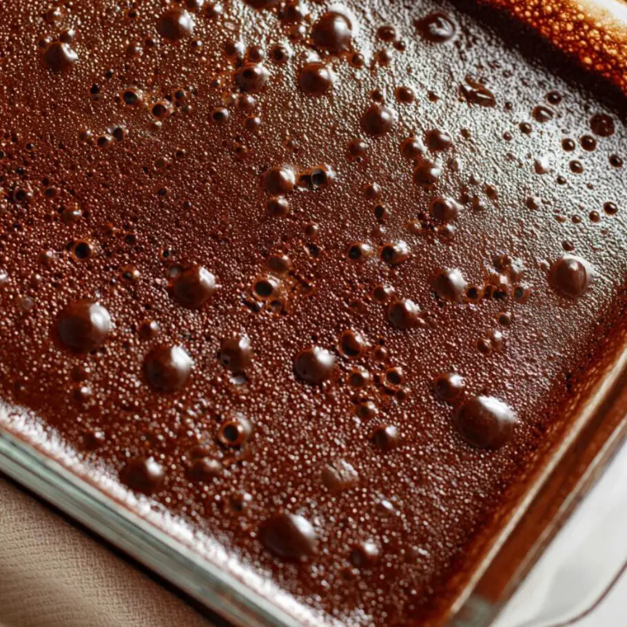 Pudding being spread over a poked chocolate cake with a spatula