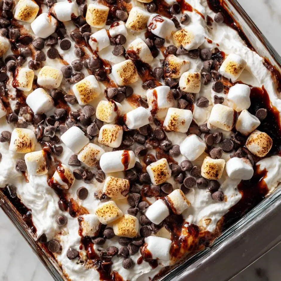 Cake topped with whipped cream, marshmallows, chocolate chips, and fudge drizzle