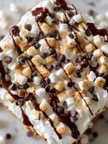 Hot cocoa poke cake recipe topped with marshmallows and chocolate drizzle on a white counter