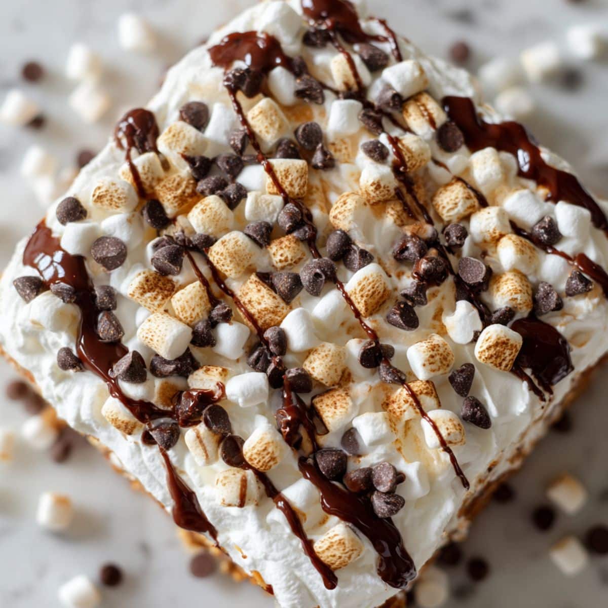 Hot cocoa poke cake recipe topped with marshmallows and chocolate drizzle on a white counter