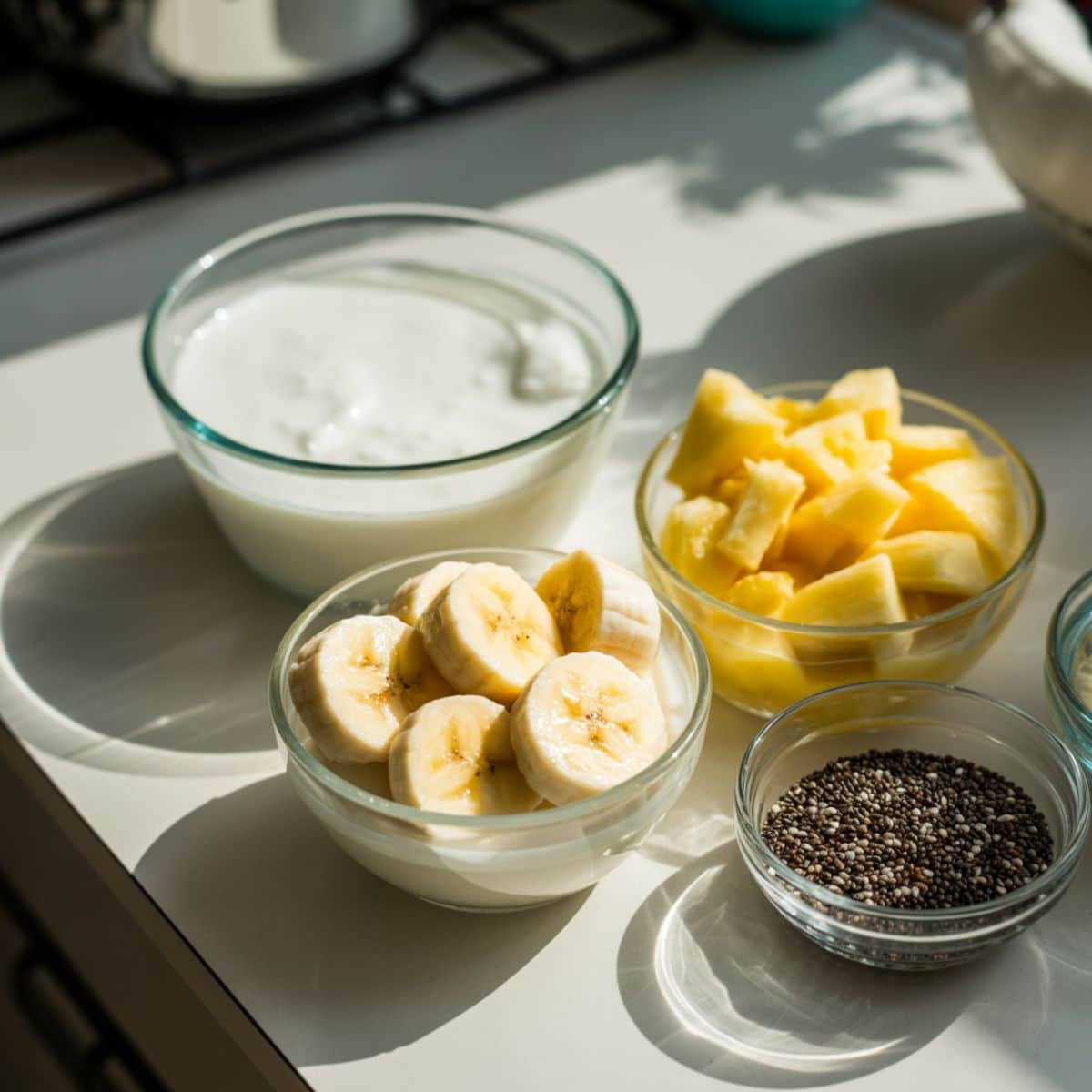 Coconut cream, banana, pineapple chunks, chia seeds, and coconut milk arranged on a counter