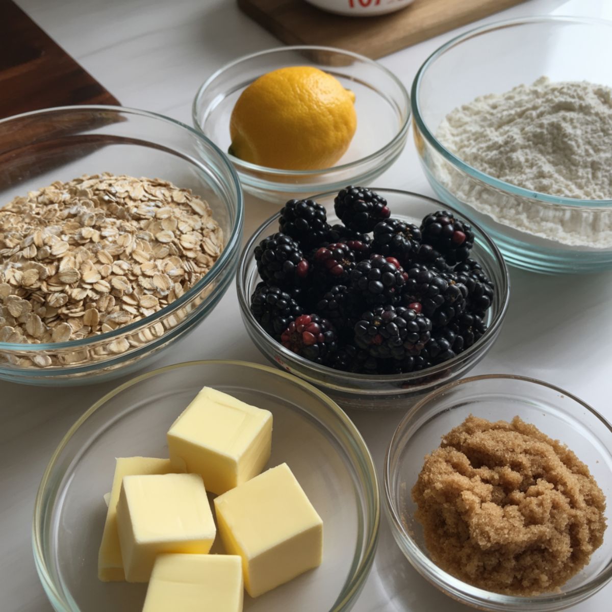 Rolled oats, blackberries, butter, and flour arranged casually on a white kitchen counter for baking.