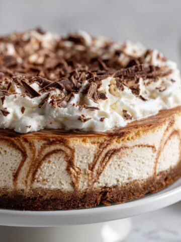 Close-up of homemade mocha cheesecake recipe with whipped topping and chocolate shavings on white kitchen counter
