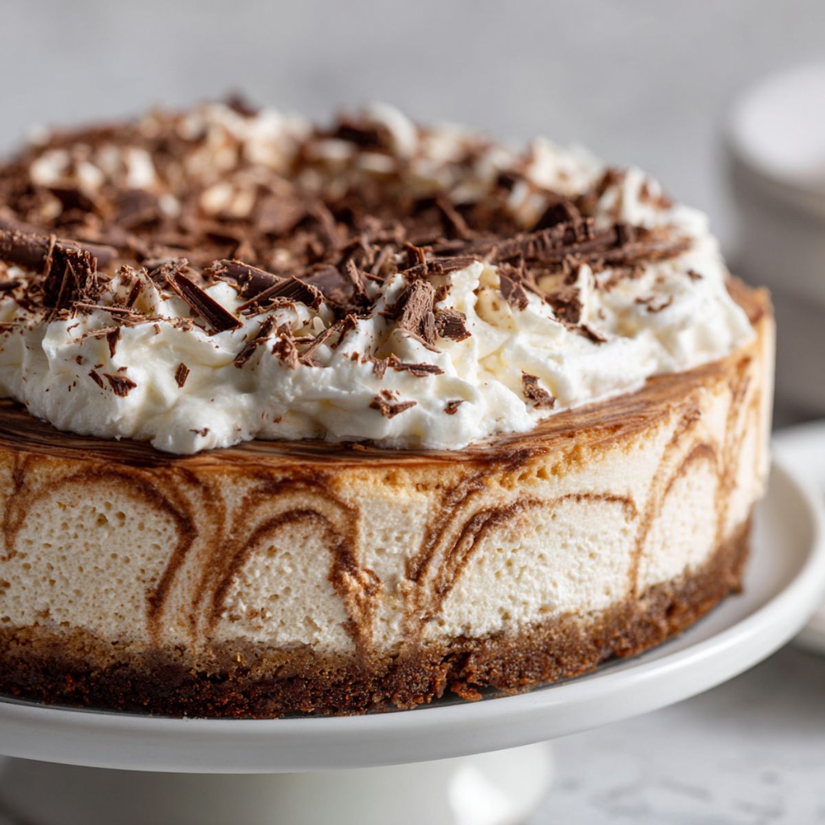 Close-up of homemade mocha cheesecake recipe with whipped topping and chocolate shavings on white kitchen counter