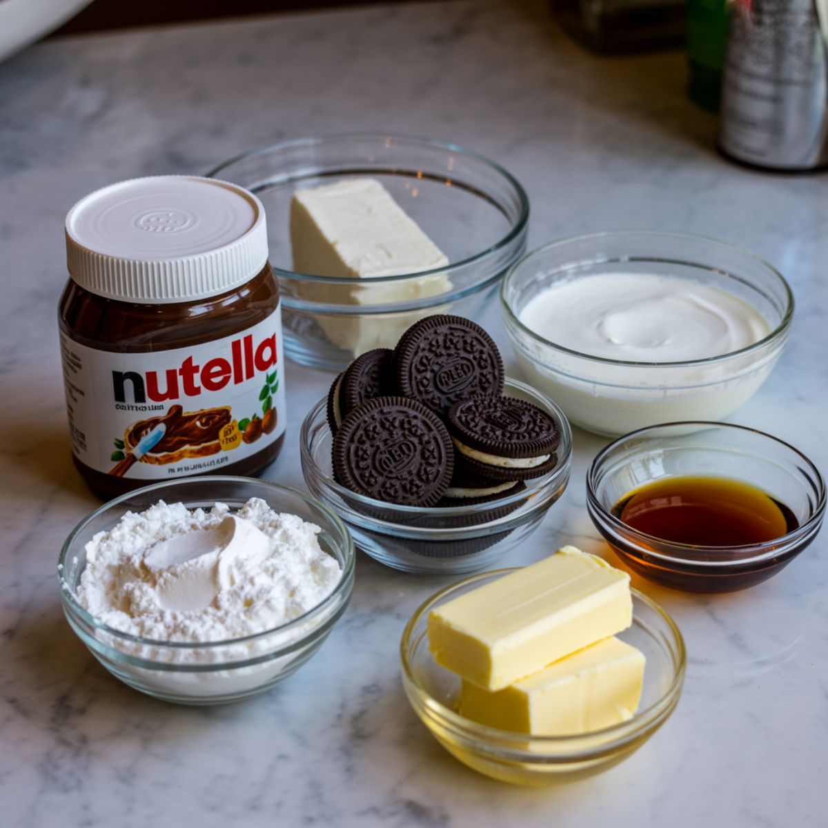 Ingredients for Nutella pie laid out on a white kitchen counter, including Nutella, cream cheese, and Oreo cookies.