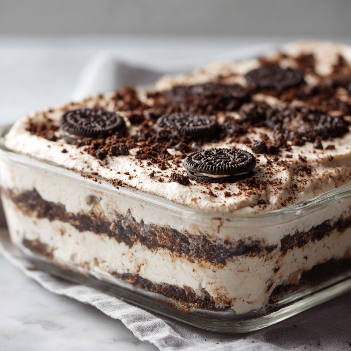 Overhead view of a chilled Oreo icebox cake recipe in a glass dish, topped with crushed Oreos