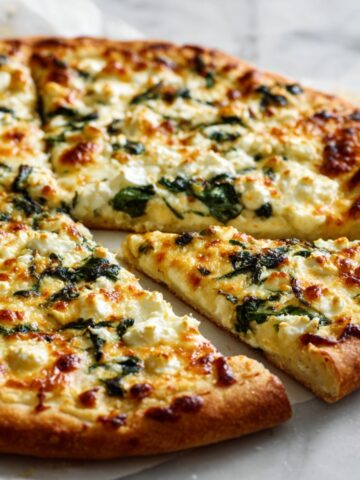Freshly baked homemade spinach and feta pizza recipe sliced on white marble countertop