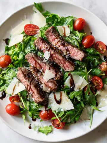 Steak and arugula salad recipe with cherry tomatoes and balsamic on a white plate