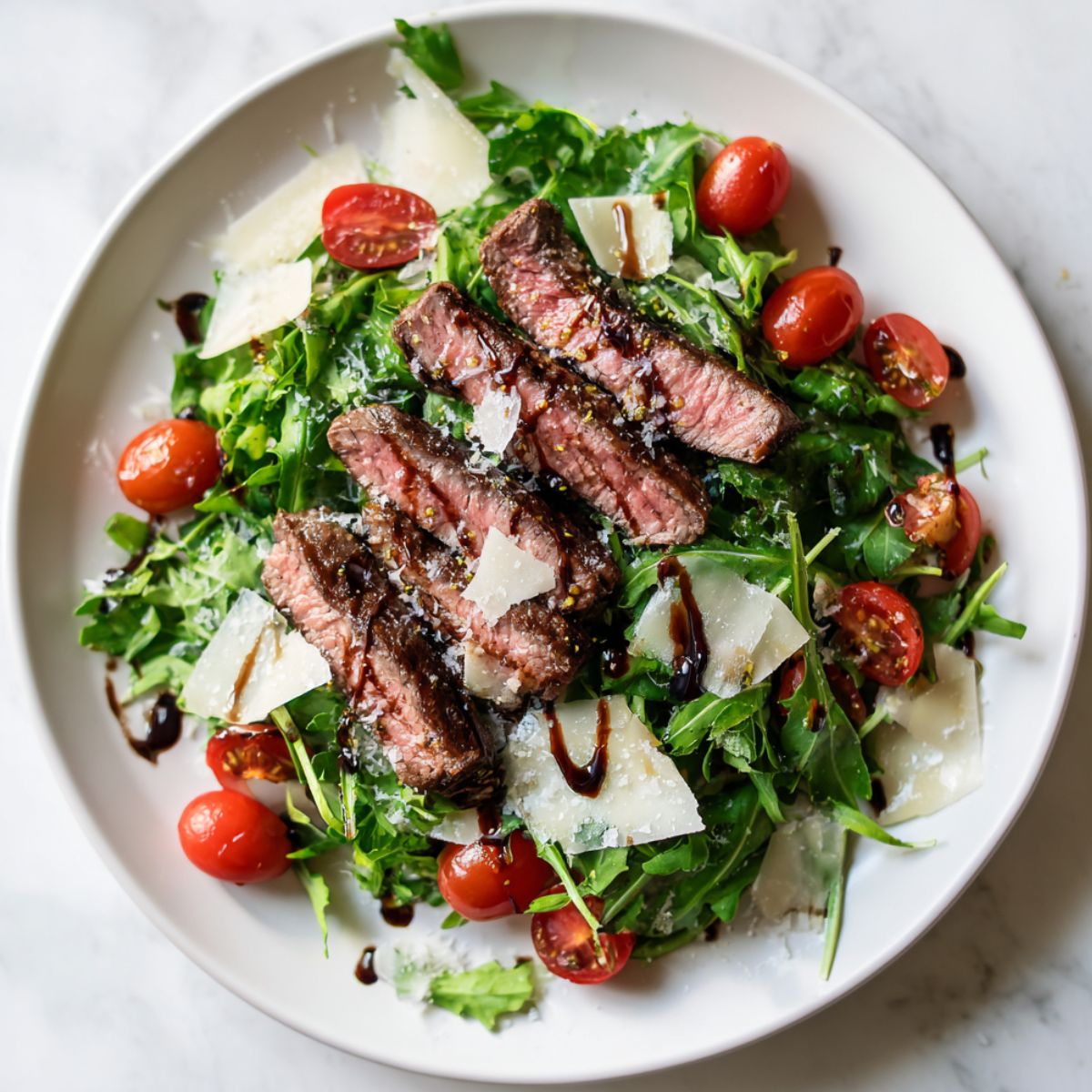 Steak and arugula salad recipe with cherry tomatoes and balsamic on a white plate

