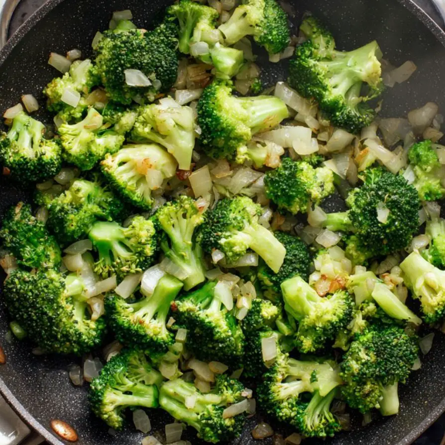 Broccoli, onions, and garlic sautéing in a pan.