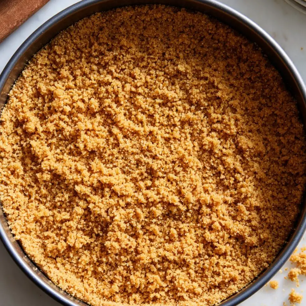 Graham cracker crust being pressed into a pan with crumbs around


